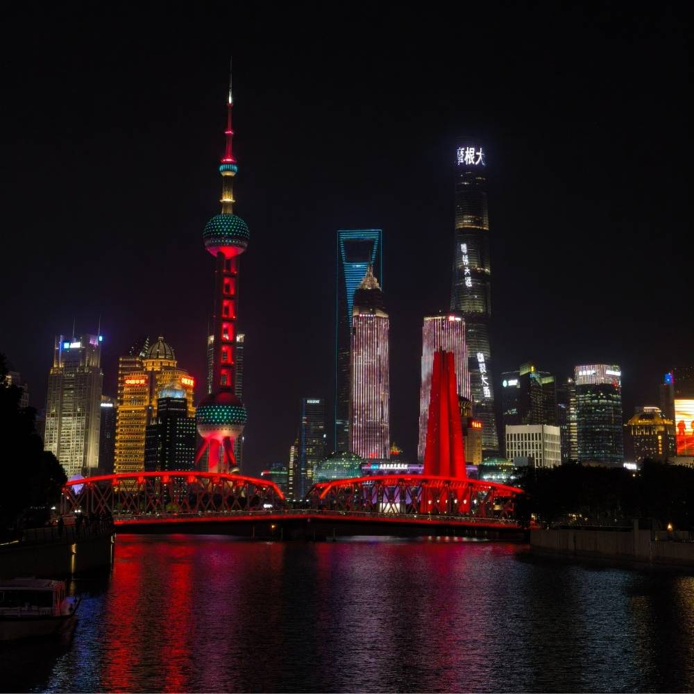 Beleuchtete Skyline von Pudong in Shanghai bei Nacht mit dem Oriental Pearl Tower und der roten Waibaidu-Br&uuml;cke &ndash; symbolischer Abschluss der China Unternehmer-Reise.