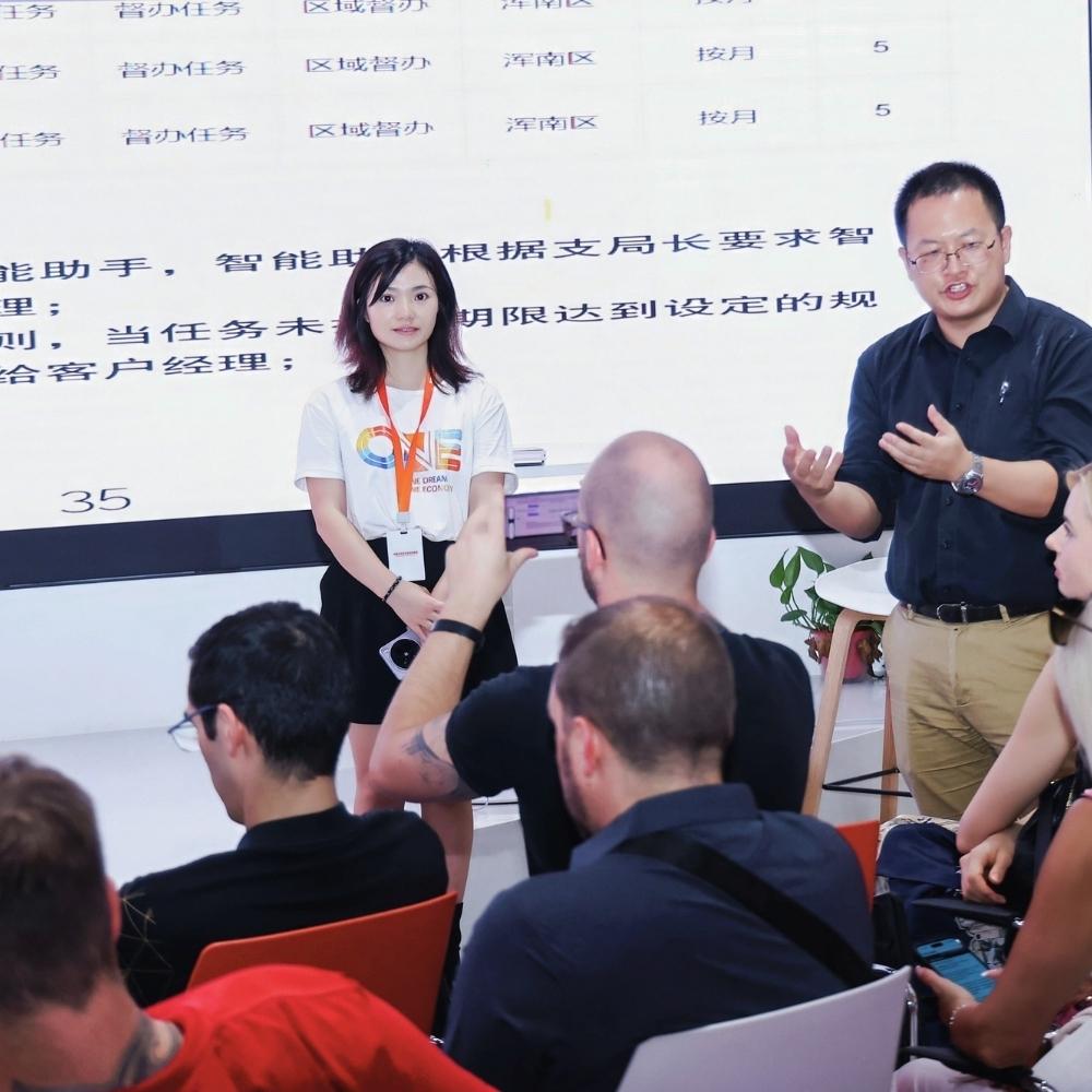 Experten-Vortrag bei Alibaba in Hangzhou. Ein Sprecher und eine Sprecherin pr&auml;sentieren digitale Strategien und Plattform-&Ouml;konomie vor einer Gruppe deutscher Unternehmer.
