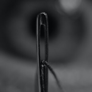 Ein Nadelöhr auf schwarzem Grund, symbolisiert die Engpässe, die durch Prozessoptimierung gelöst werden sollten. Was sich jedoch oft als Herausforderung entpuppt.