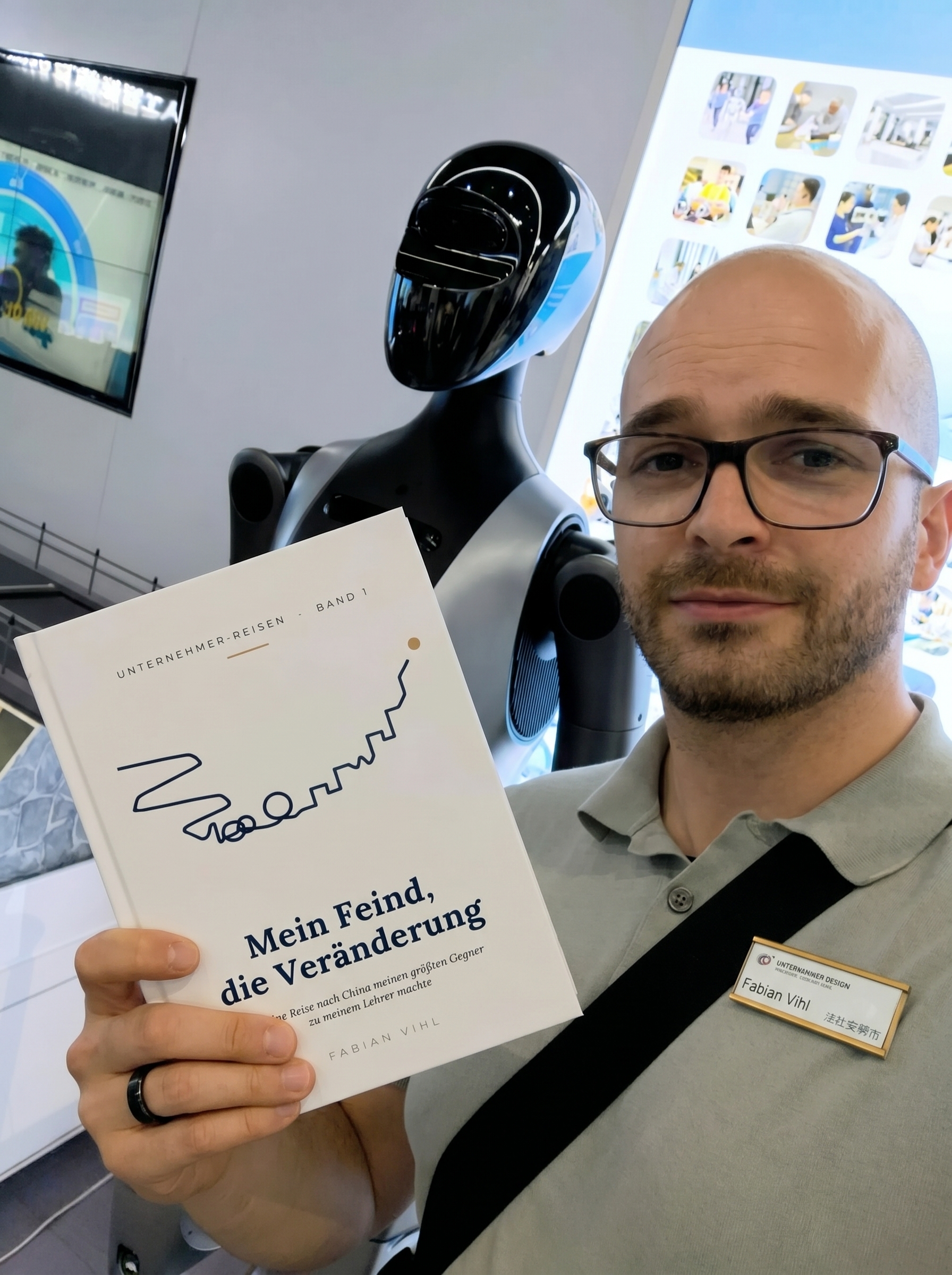 Fabian Vihl mit humanoidem Roboter bei UBTECH in Shenzhen, in der Hand sein Roman Mein Feind, die Veränderung